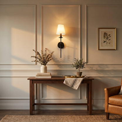 Classic American wall sconce in matte black with white fabric shade, mounted on a panelled wall above a walnut console table