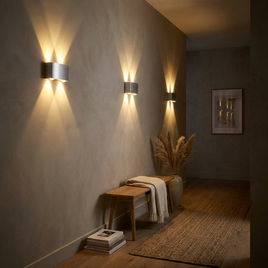 Three aluminium up and down wall lights in a row along a warm plaster corridor wall at night